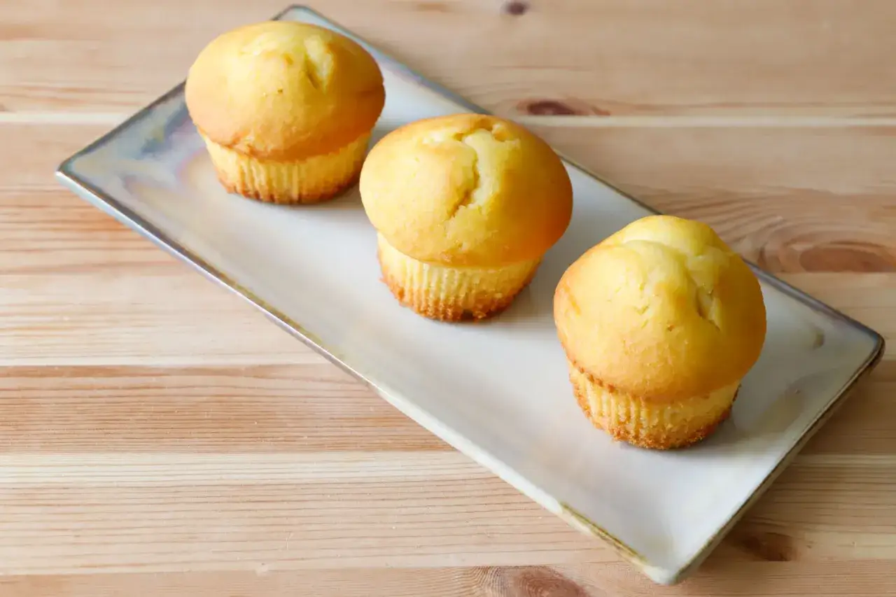 Tre soffici muffin allo yogurt dorati, serviti su un piatto rettangolare su un tavolo di legno.