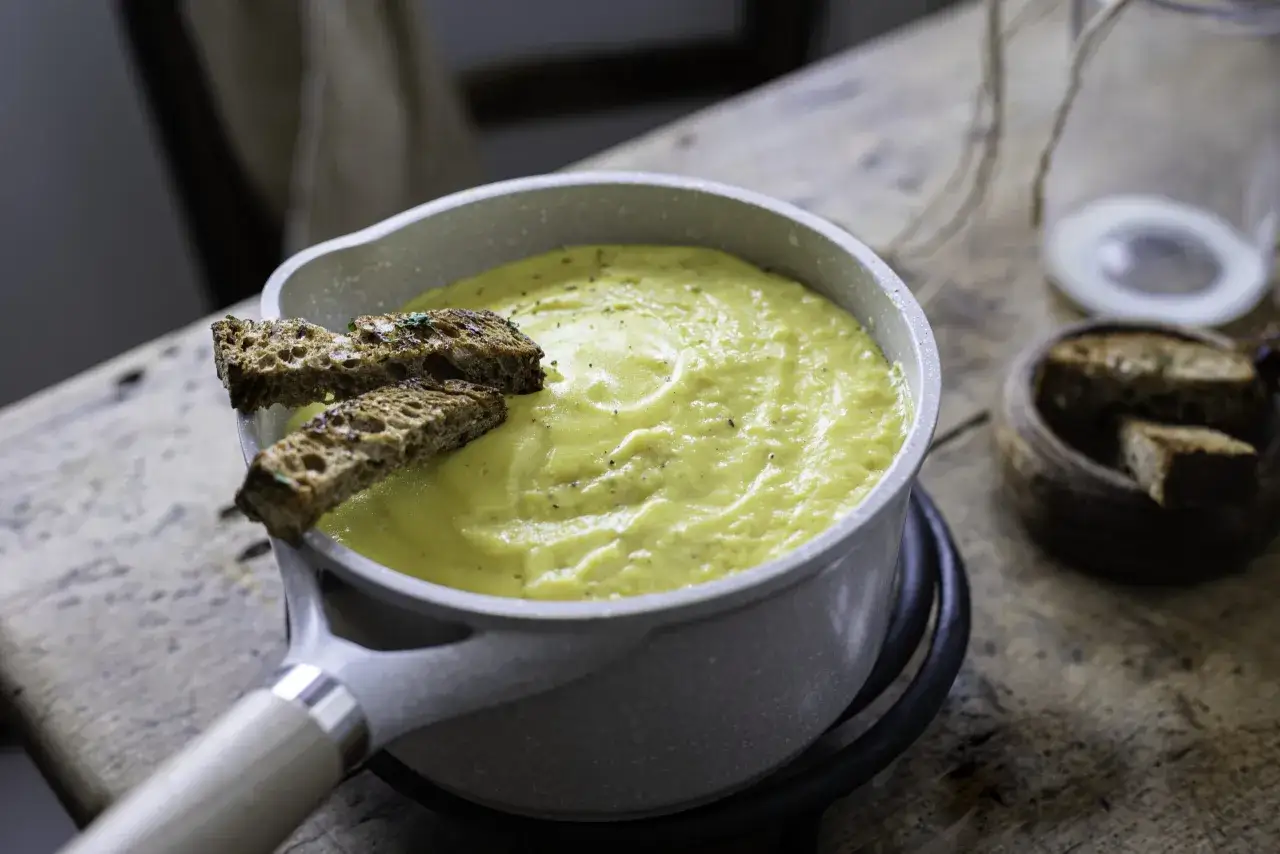 Crema gialla e vellutata, una besciamella senza glutine, servita in una pentola con crostini di pane tostato.