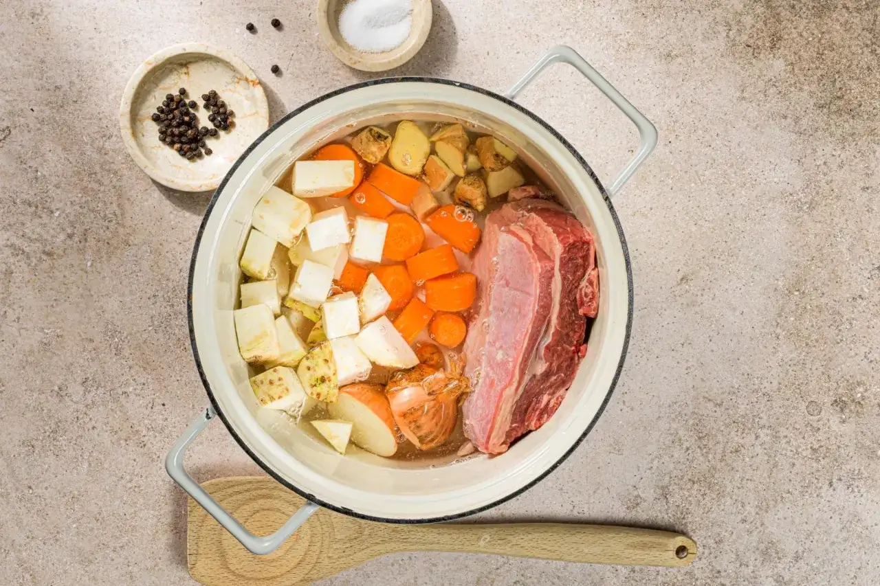 Carne, carote, sedano e cipolla in pentola per un saporito brodo di carne. Peperoncini e sale a lato.