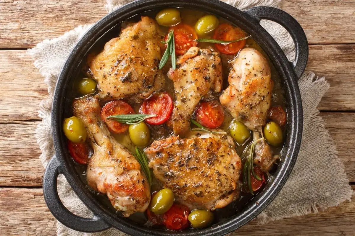 Un saporito pollo alla mediterranea in padella, con pomodorini, olive verdi e rosmarino su un letto di lino grezzo.