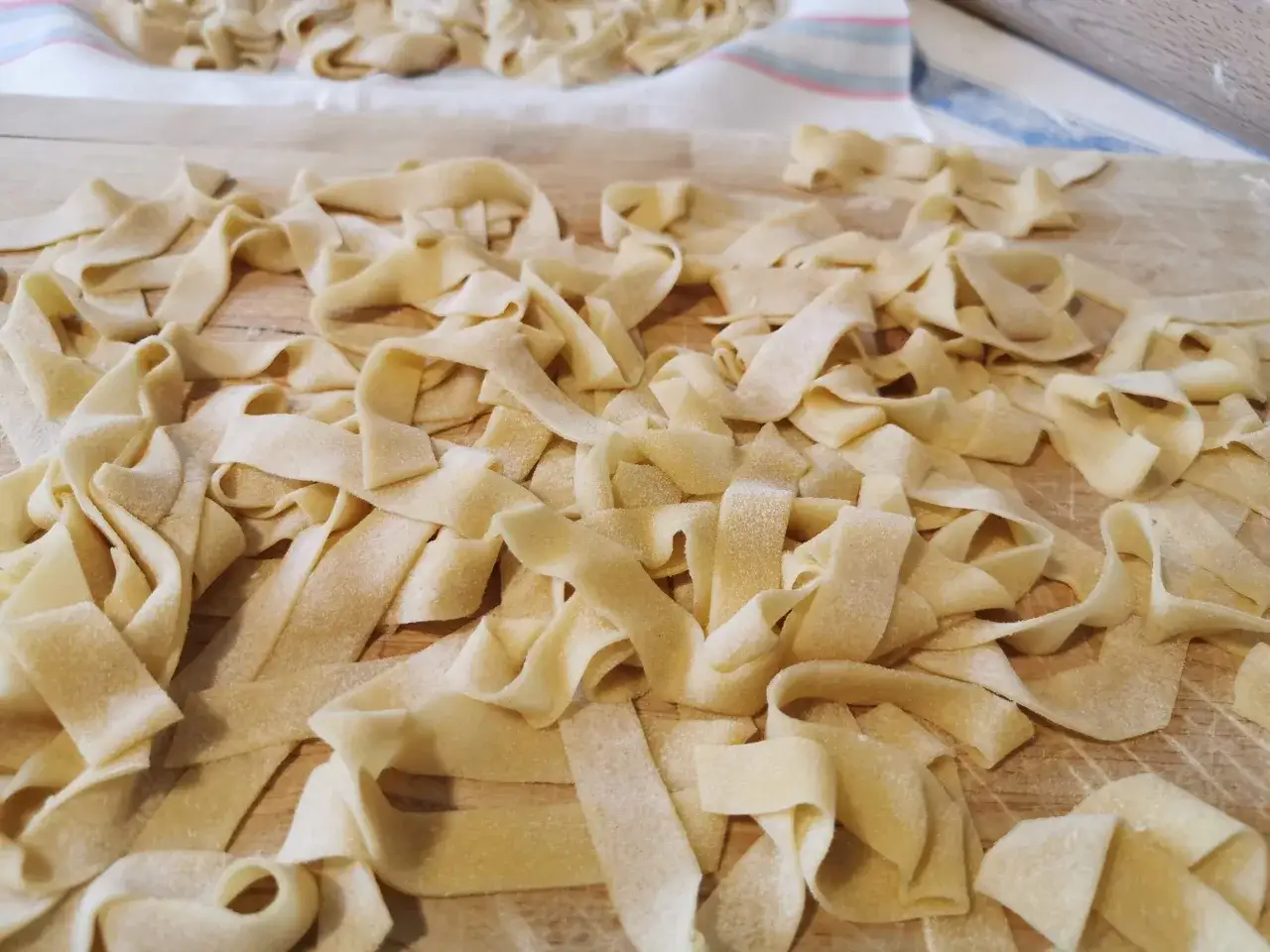 Fettuccine fresche, tagliatelle fatte in casa sparse su un tagliere di legno, pronte per essere cucinate.