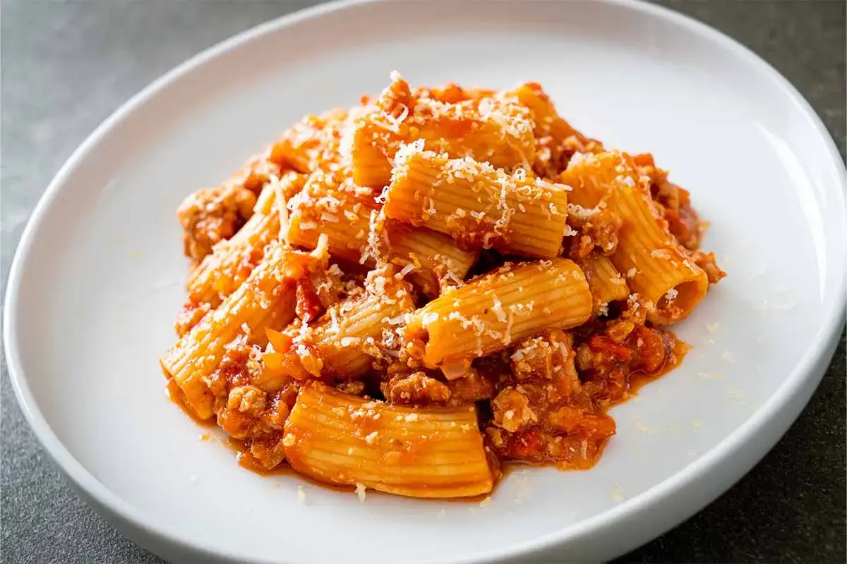Piatto di pasta alla zozzona con rag&ugrave; ricco e abbondante parmigiano grattugiato, servita su un piatto bianco.