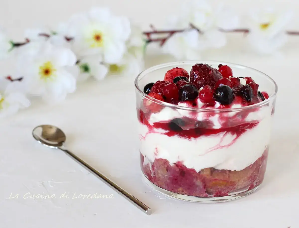 Deliziosa panna cotta con frutti di bosco freschi e una salsa rossa, servita in un bicchiere con un cucchiaino.