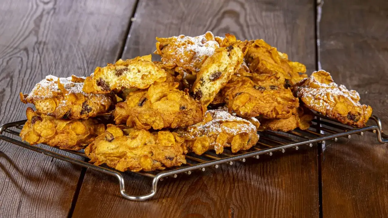 Un mucchio di croccanti biscotti alle corn flakes e uvetta, spolverati di zucchero a velo, sembrano piccole rose del deserto su una griglia.