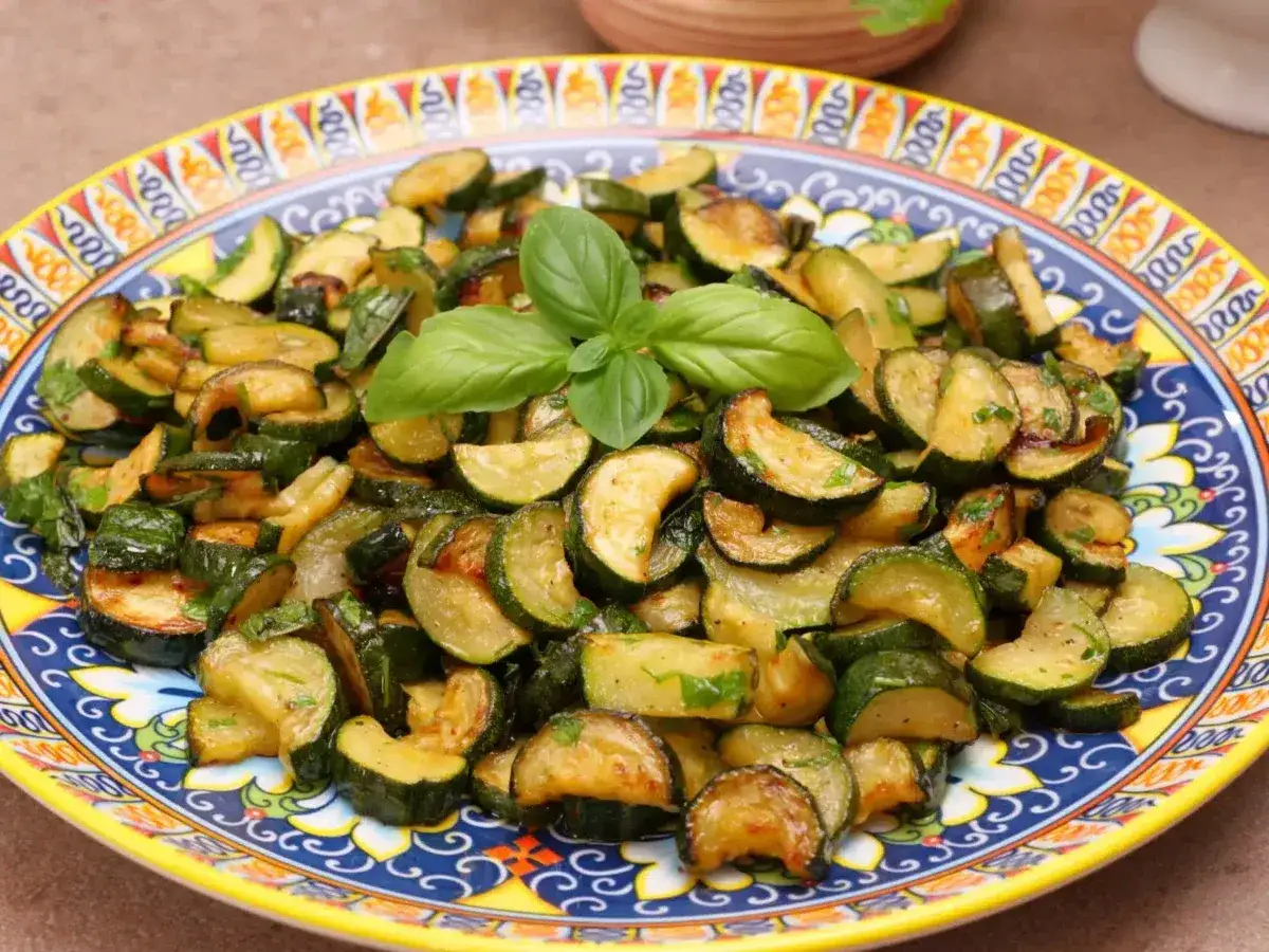 Zucchine trifolate dorate e saporite, guarnite con basilico fresco, servite su un piatto decorato.