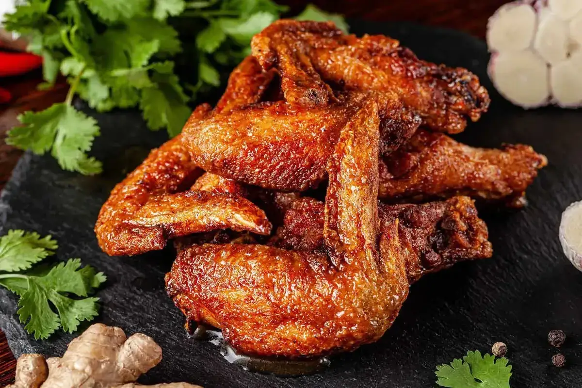 Alette di pollo dorate e succulente, servite su una pietra scura con zenzero, aglio e coriandolo fresco.