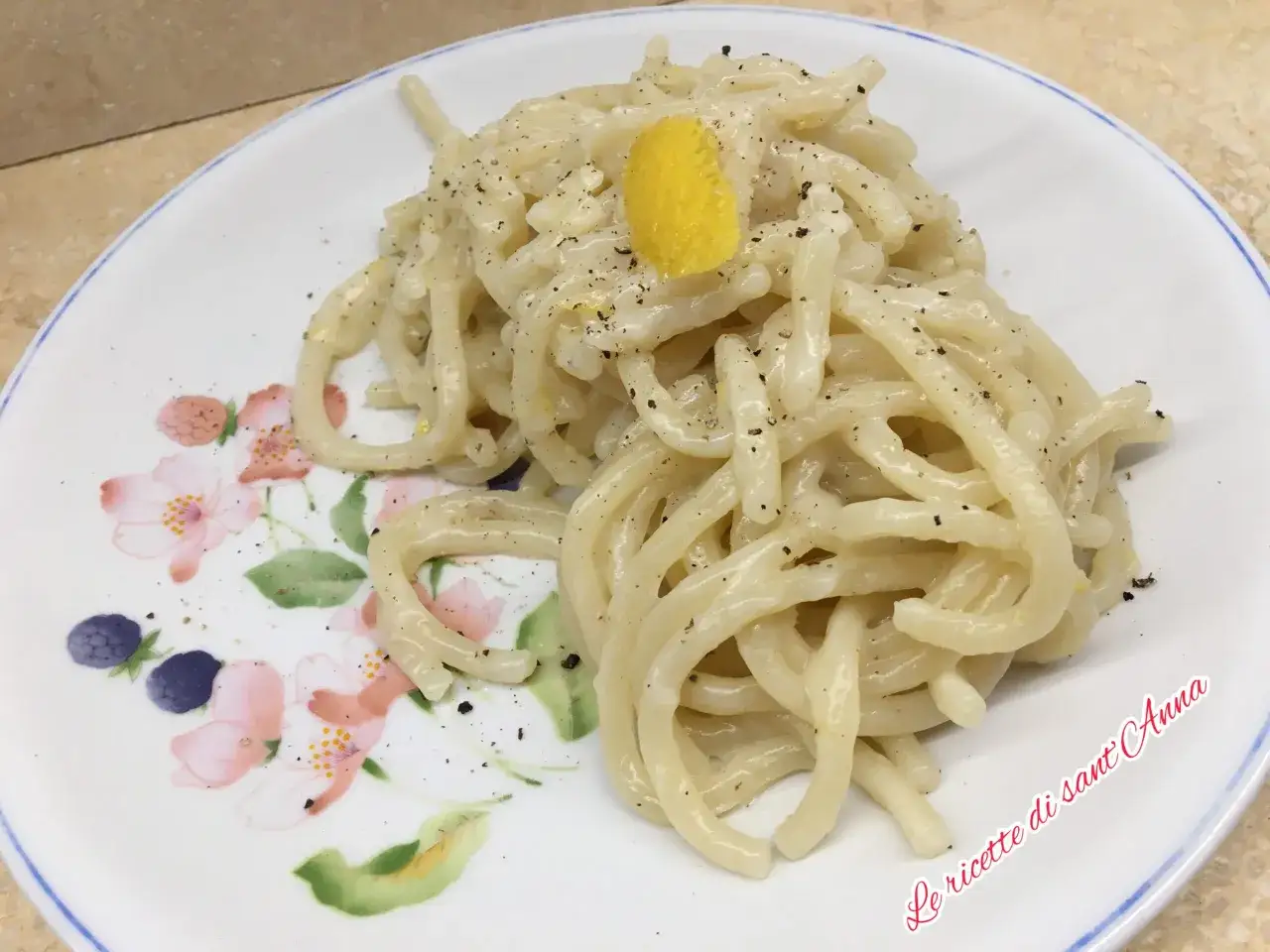 Un piatto di spaghetti al limone, cremosi e profumati, guarniti con una scorzetta gialla e pepe nero.