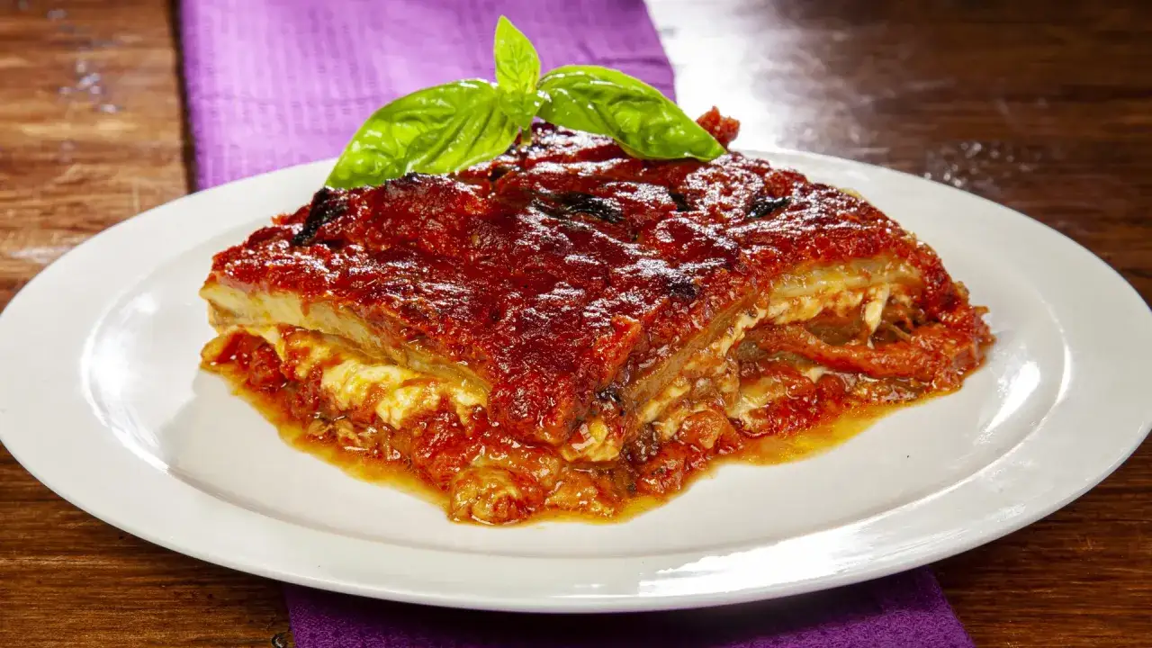 Una fetta di parmigiana di melanzane non fritte, ricca di sugo e formaggio, guarnita con basilico fresco.
