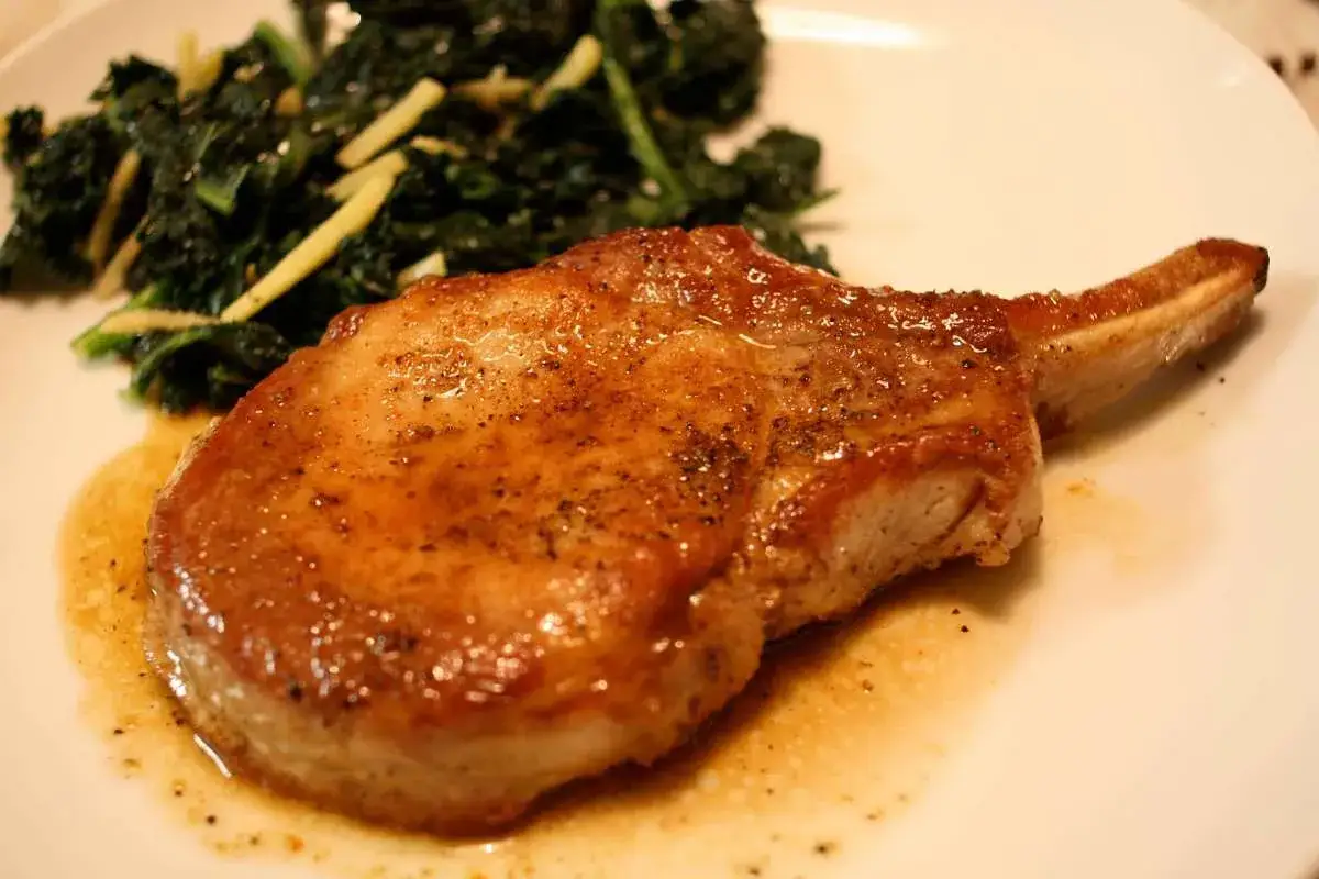 Succulenta braciola di maiale dorata, servita con verdure verdi saltate e una salsa saporita.