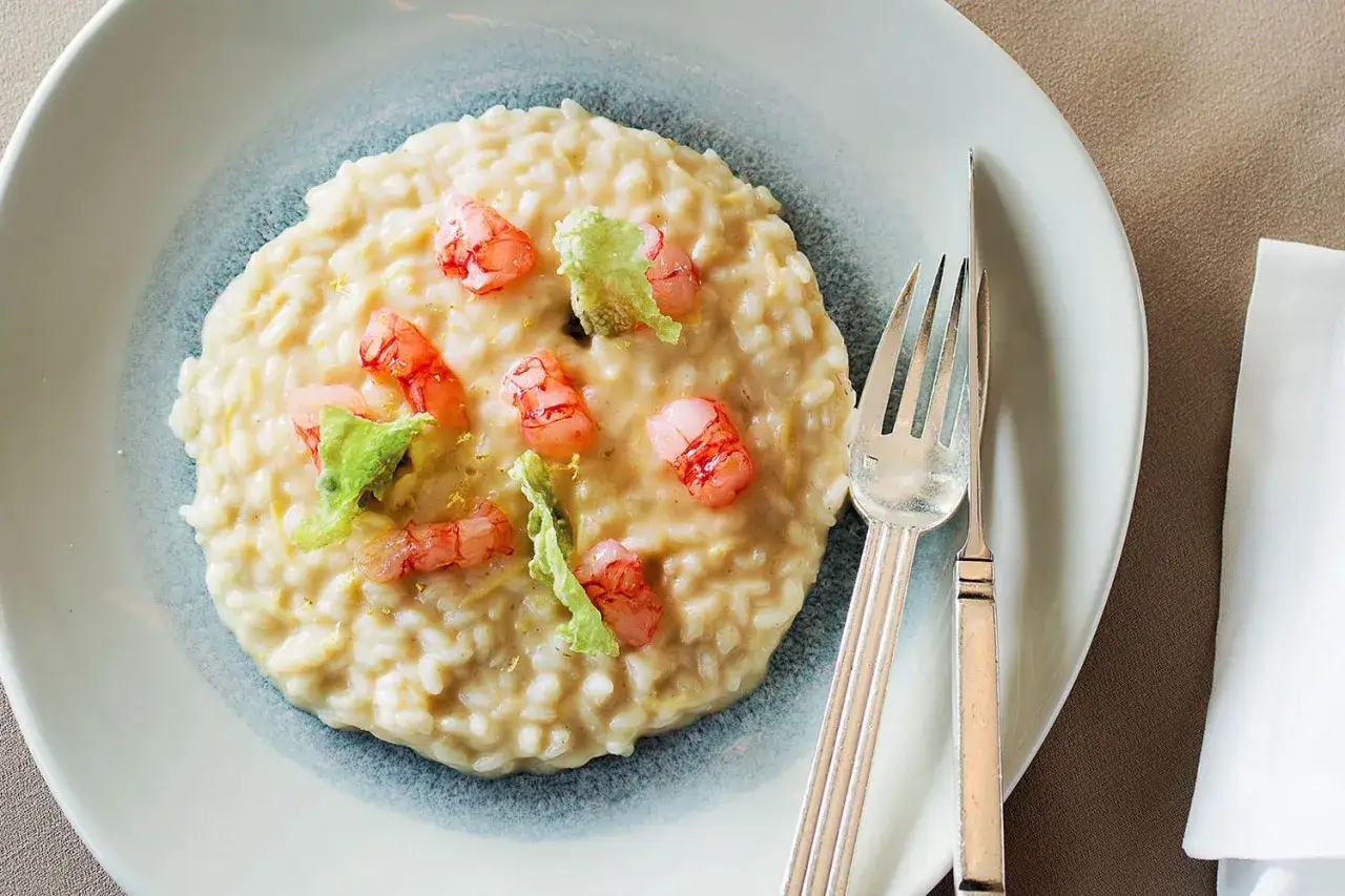 Un cremoso risotto gamberi e limone, guarnito con gamberetti rosa e scorza di limone grattugiata, pronto per essere gustato.