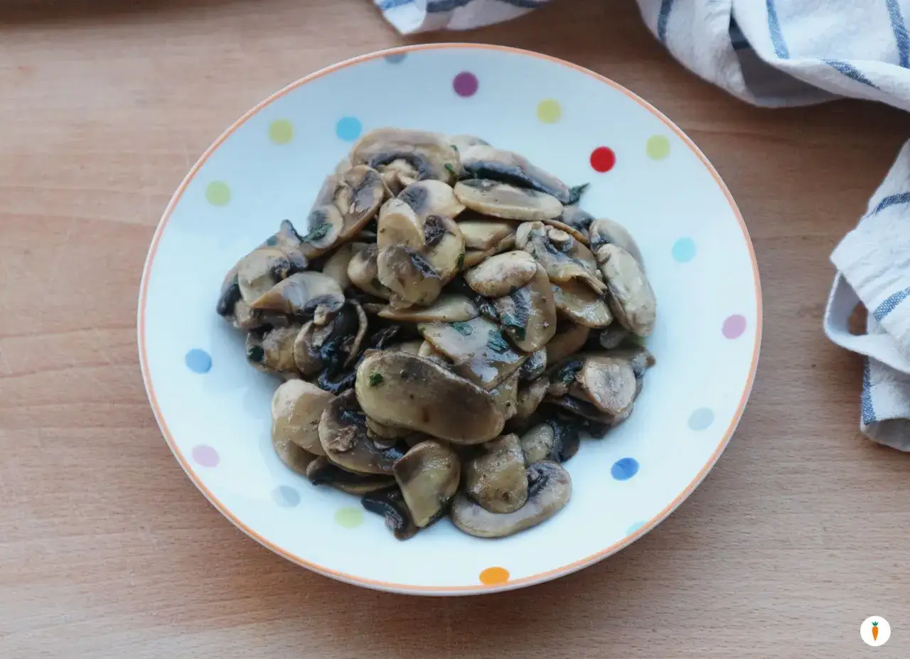 Funghi in padella, saporiti e profumati, serviti su un piatto bianco a pois colorati.