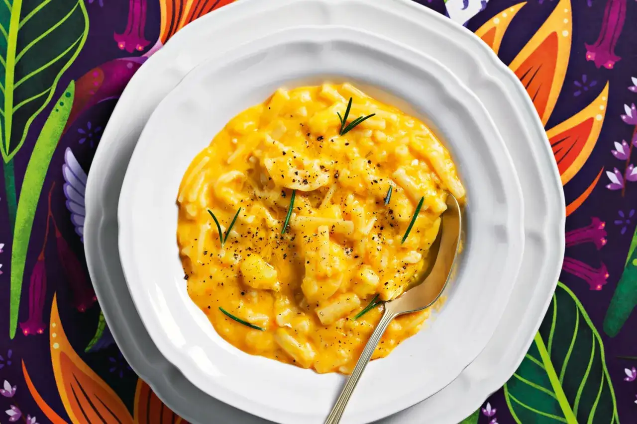 Un piatto invitante di pasta con patate cremosa, guarnita con rosmarino e pepe nero, servita su un piatto bianco con un cucchiaio dorato.