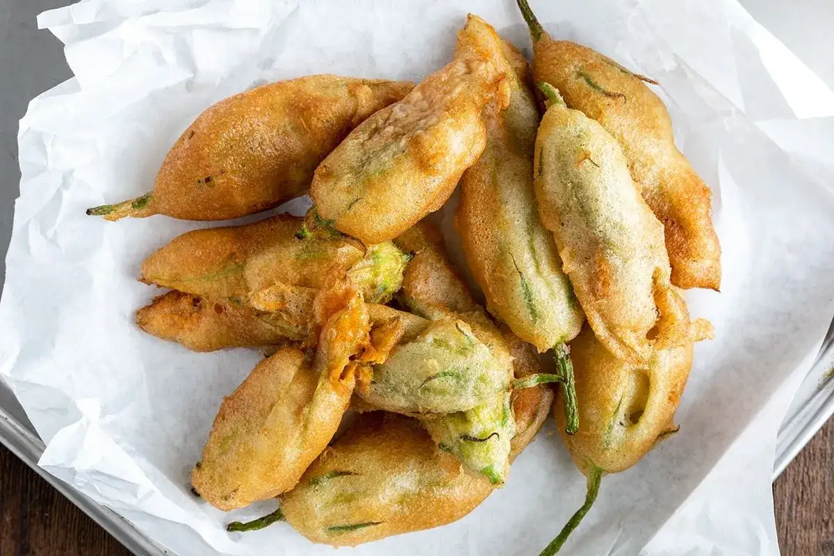 Un mucchio di fiori di zucca fritti, dorati e croccanti, adagiati su carta bianca.