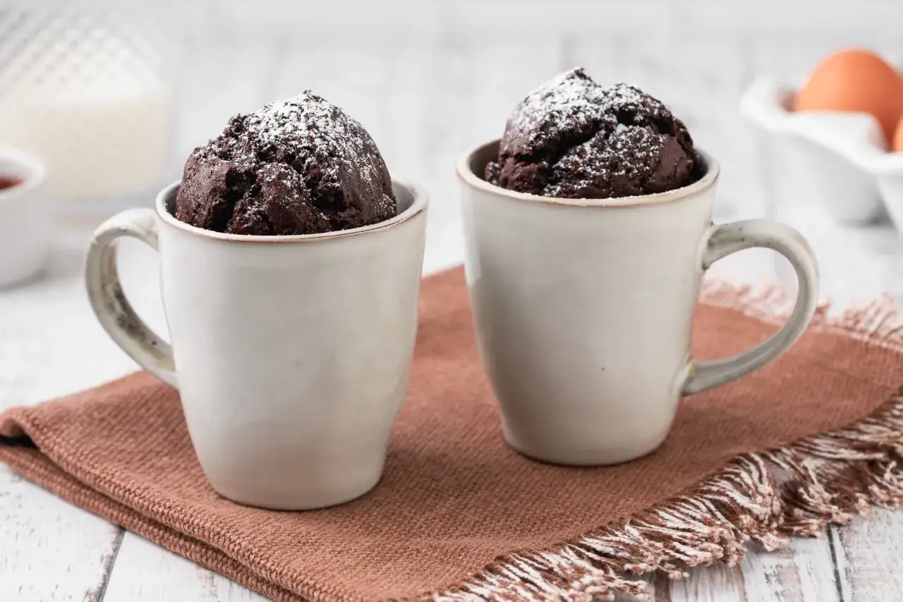 Due tortine al cioccolato in tazza, spolverate di zucchero a velo, pronte per essere gustate. Una deliziosa torta in tazza al microonde.