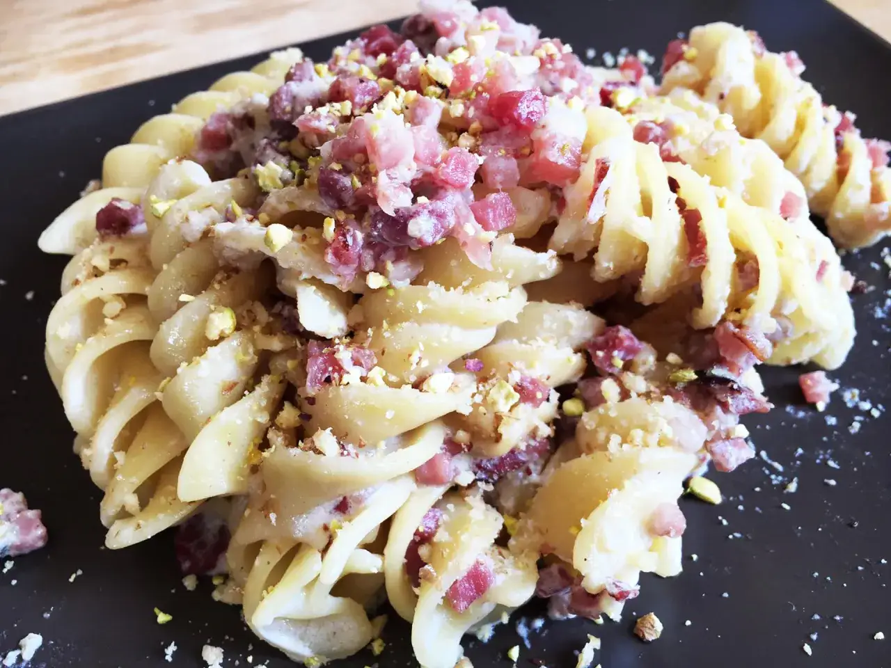 Fusilli cremosi con panna, speck croccante e granella di pistacchi. Un piatto invitante e saporito.