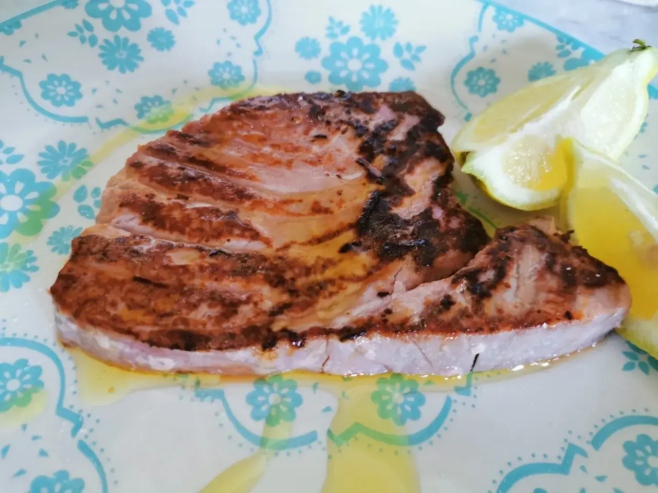 Bistecca di tonno fresco grigliata, succosa e dorata, servita con spicchi di limone su un piatto decorato. Un'idea per come cucinare il tonno fresco.