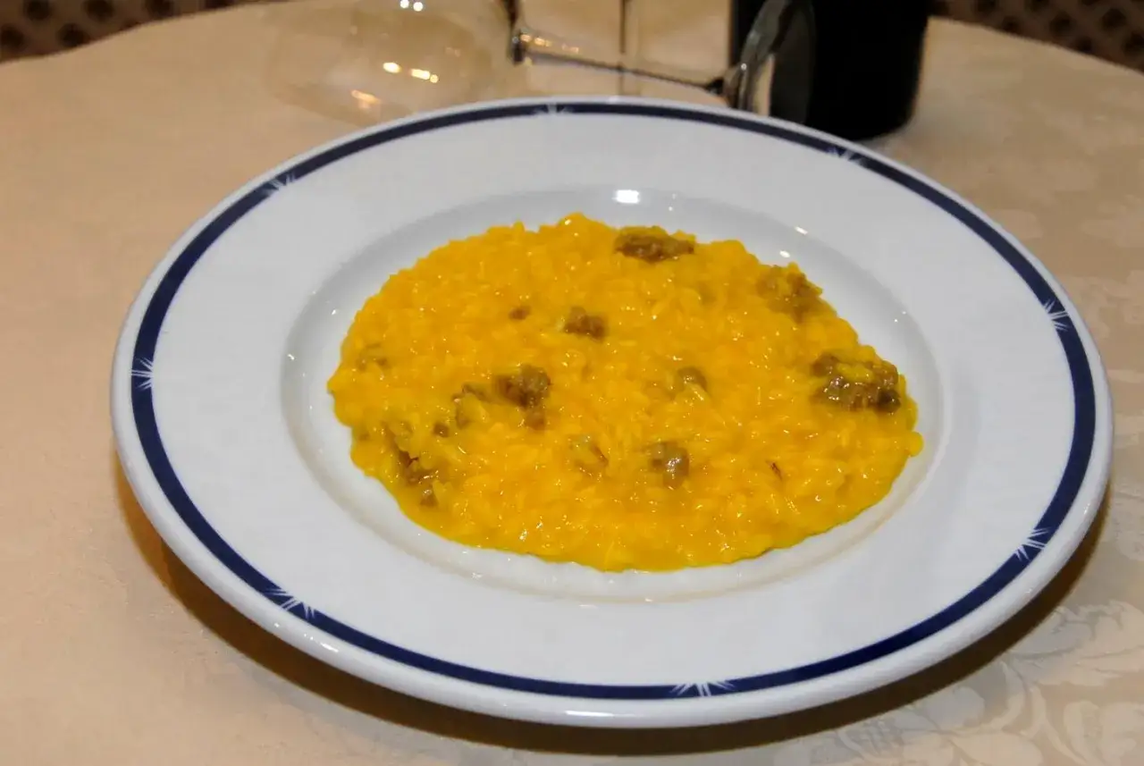 Un invitante risotto alla monzese, cremoso e dal colore dorato, servito su un piatto bianco con bordo blu.