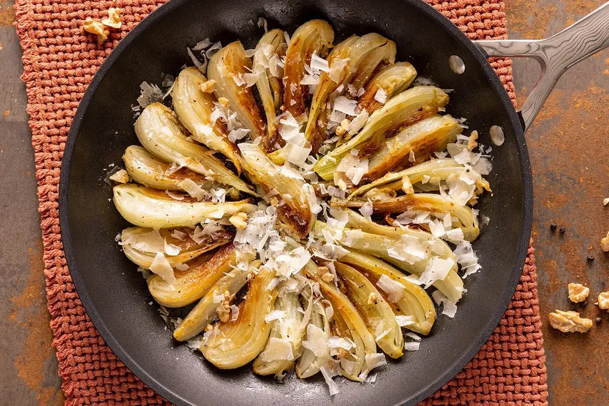 Finocchi in padella dorati, guarniti con scaglie di formaggio e noci croccanti. Un contorno saporito e invitante.