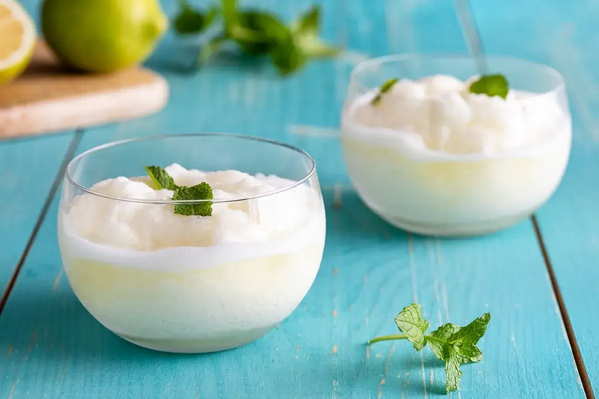 Due bicchieri di sorbetto al limone veloce, guarniti con menta fresca, su un tavolo di legno blu.
