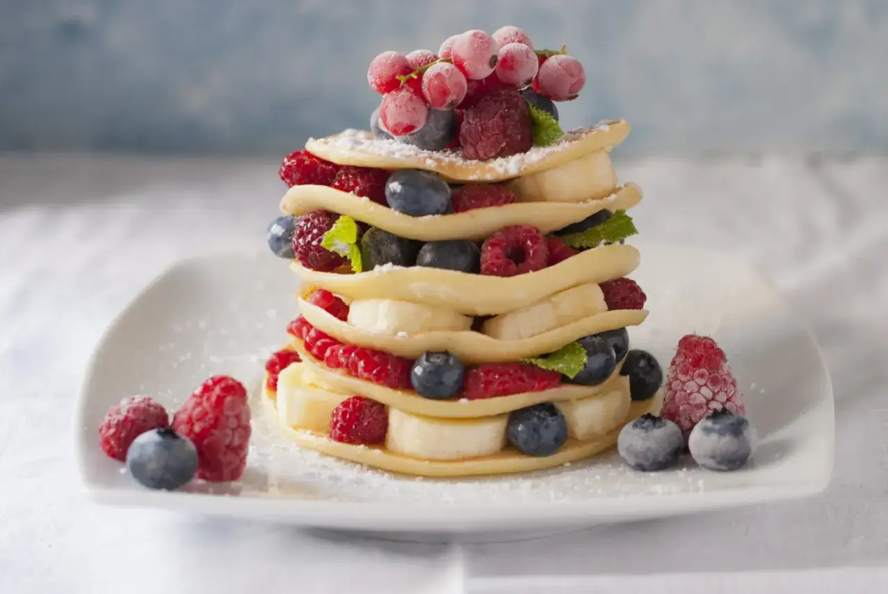 Un pancake light a strati, decorato con lamponi, mirtilli, fette di banana e ribes rosso.