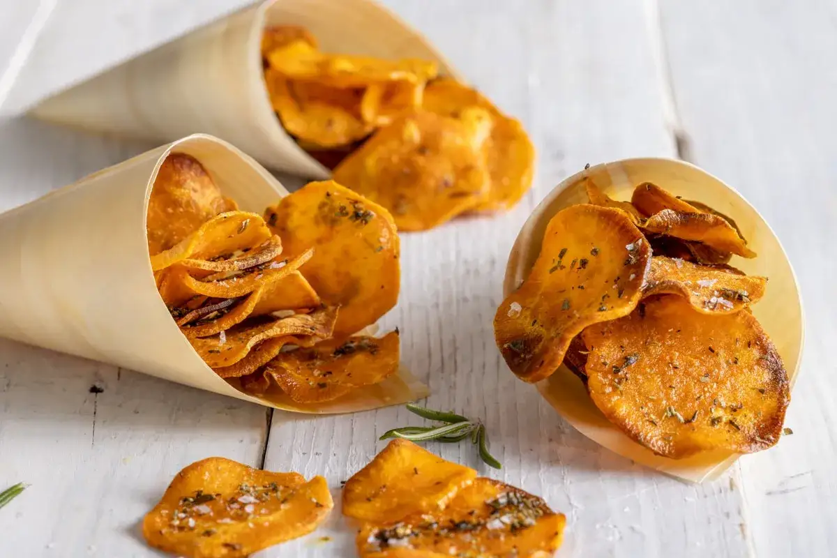 Croccanti patate dolci in padella, condite con erbe aromatiche e sale, servite in coni di legno.