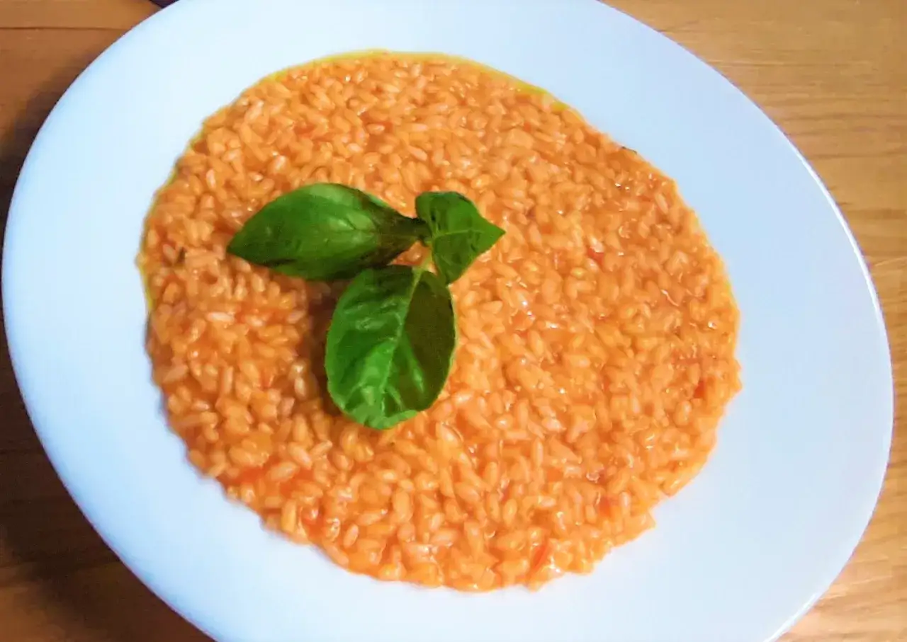 Un cremoso risotto al pomodoro, arricchito da foglie di basilico fresco, pronto per essere gustato.
