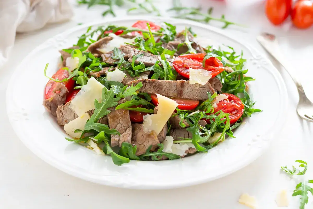 Deliziosi straccetti di vitello su un letto di rucola fresca e pomodorini, guarniti con scaglie di parmigiano.