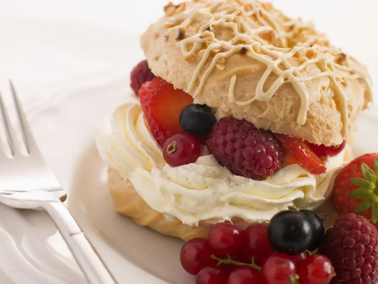 Dolce con panna montata e frutti di bosco, guarnito con glassa bianca e nocciole tritate. La crema chantilly &egrave; soffice e abbondante.