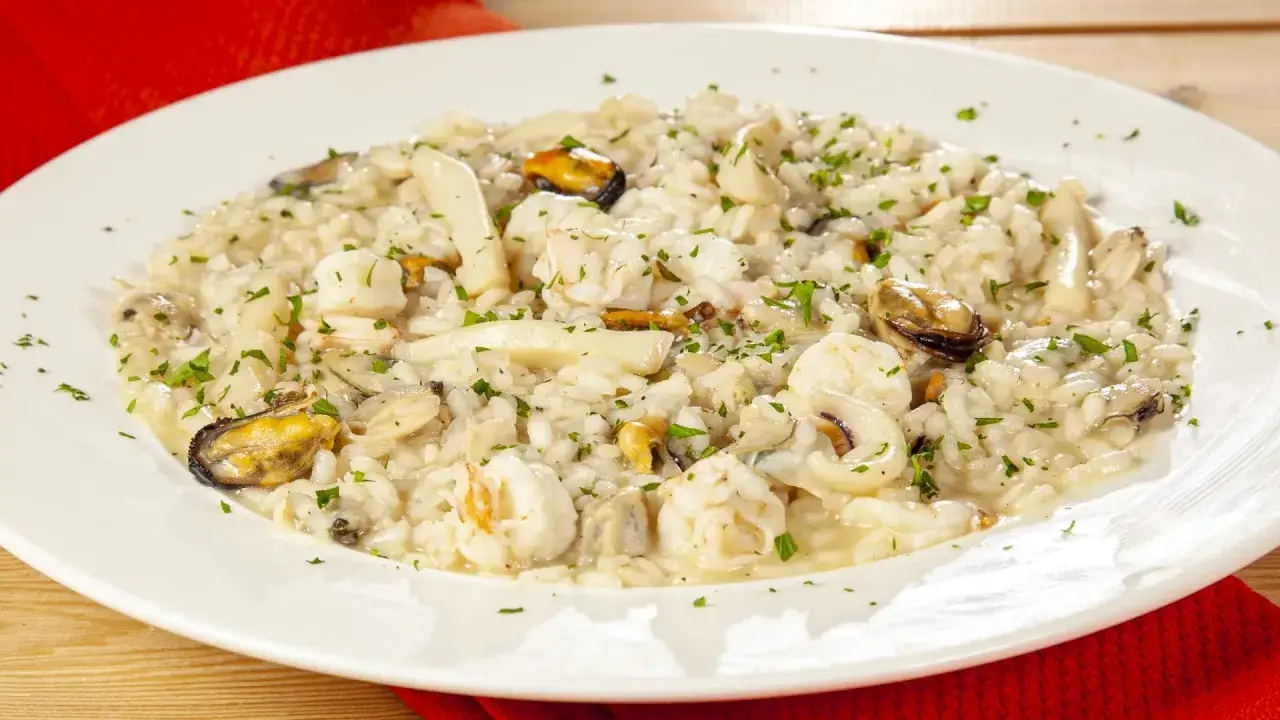 Un cremoso risotto allo scoglio, ricco di gamberi, cozze e calamari, guarnito con prezzemolo fresco.