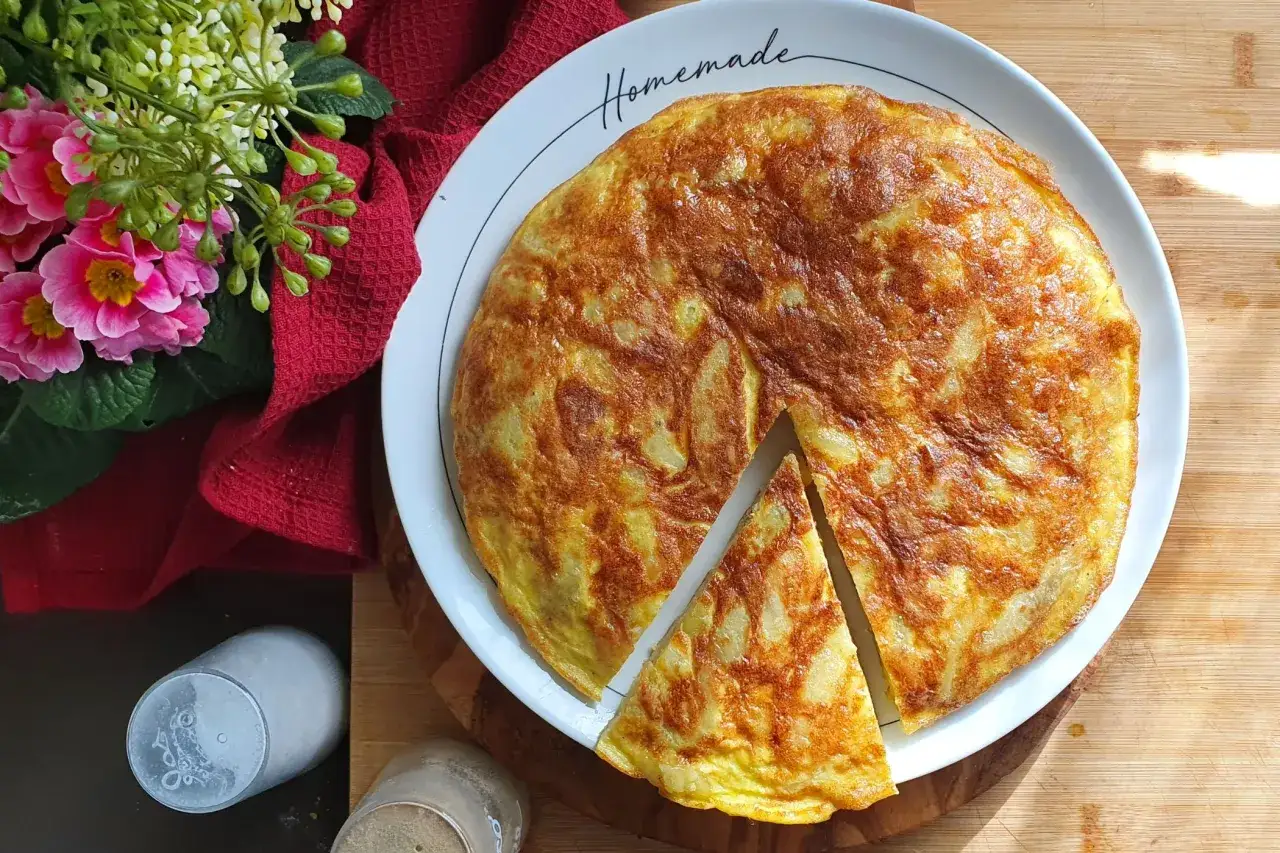 Una dorata frittata di patate, tagliata a spicchi, su un piatto con la scritta 