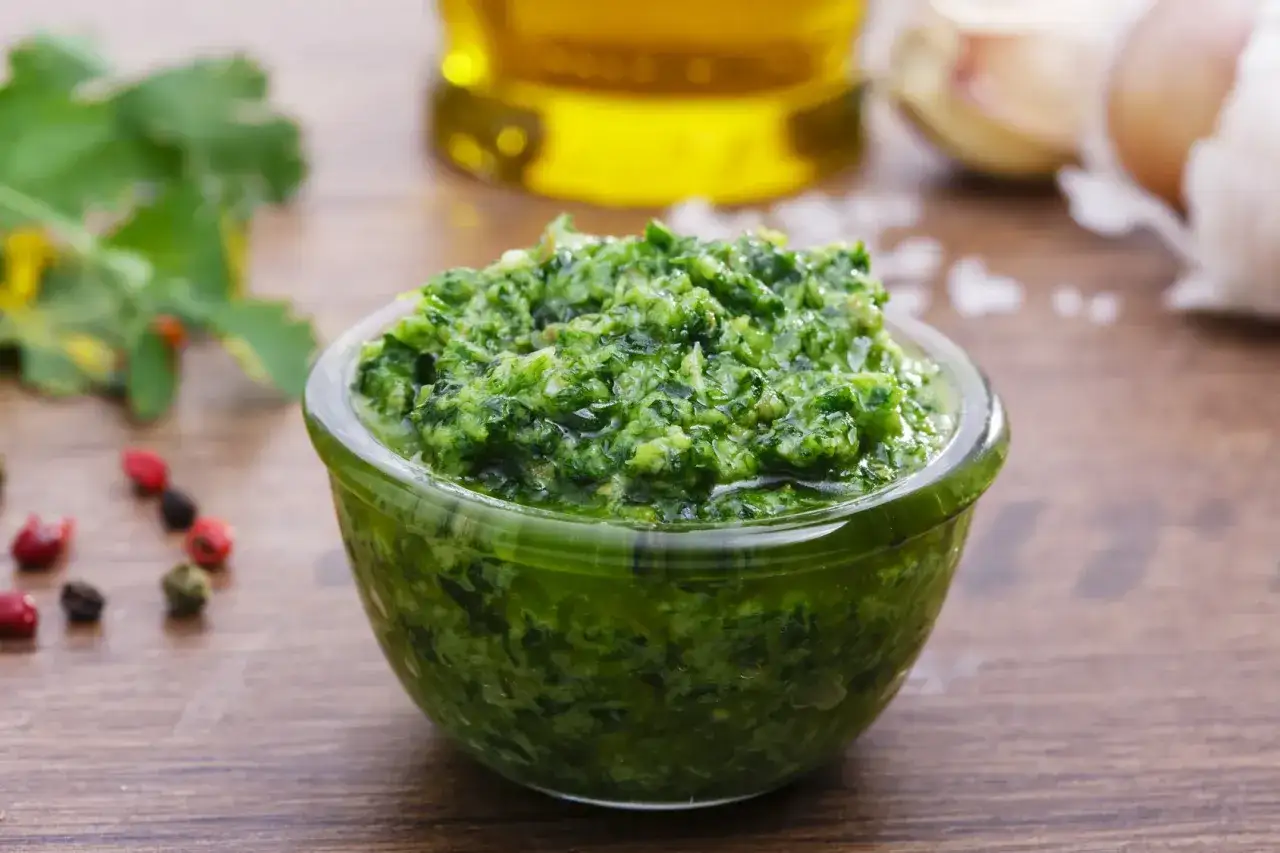 Una ciotola di vibrante salsa verde, con ingredienti freschi come aglio e pepe in sottofondo.