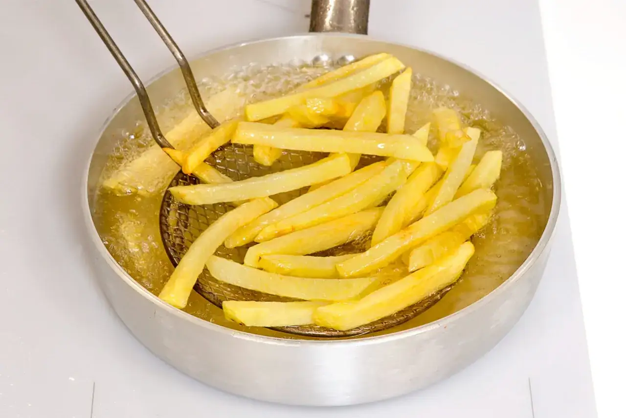 Patatine fritte dorate che sfrigolano nell'olio bollente, pronte per essere gustate.