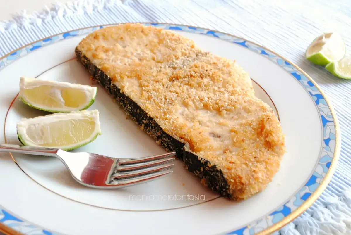 Un gustoso pesce spada impanato, cotto alla perfezione nella friggitrice ad aria, servito con spicchi di lime su un piatto elegante.