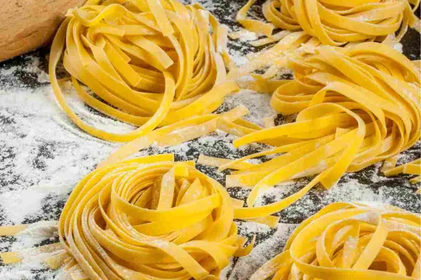 Nidi di tagliatelle fatte in casa, fresche e dorate, sparse su un piano cosparso di farina. Un invito alla tradizione culinaria.