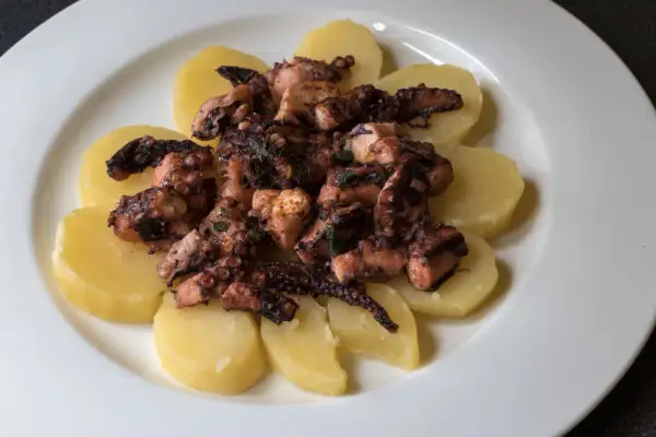 Un saporito polpo alla gallega, tagliato a pezzi e servito su fette di patate bollite, condito con erbe aromatiche.