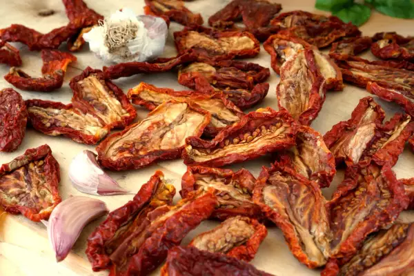 Pomodori secchi, aglio e basilico su un tagliere di legno. Un sapore intenso che evoca il sole e la terra.