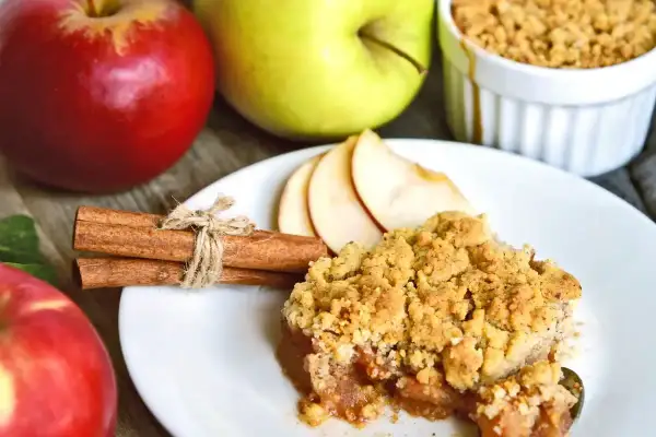 Un delizioso crumble di mele, con mele rosse e verdi sullo sfondo, cannella e fette di mela.