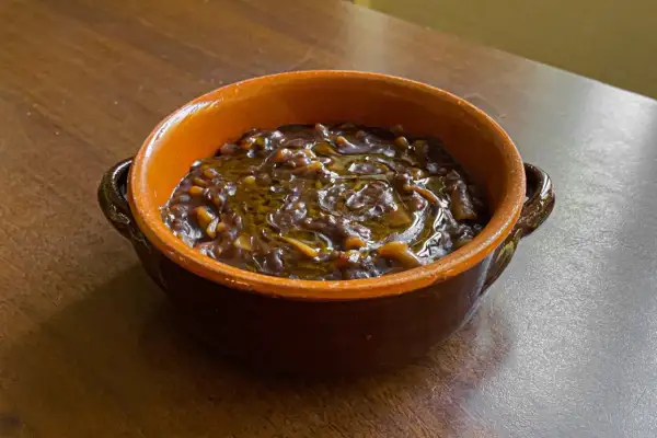 Una ciotola di terracotta piena di pasta e lenticchie, condita con olio d'oliva. Un piatto confortante e saporito.