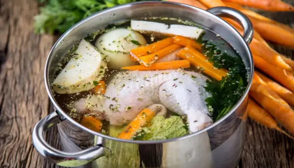 Pentola con brodo di pollo, verdure fresche e erbe aromatiche. Carote intere sullo sfondo.