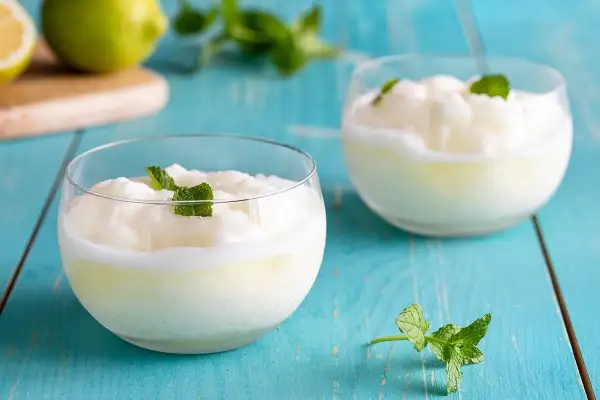 Due bicchieri di sorbetto al limone veloce, guarniti con menta fresca, su un tavolo di legno blu.