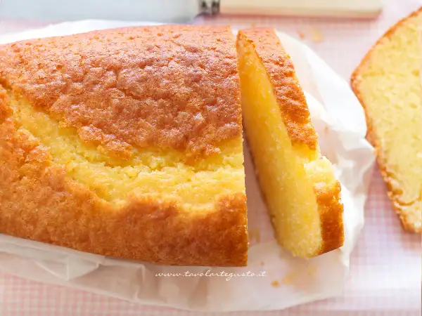 Un soffice plumcake allo yogurt, dorato e invitante, con una fetta tagliata che ne mostra la morbidezza. Perfetto per la colazione.