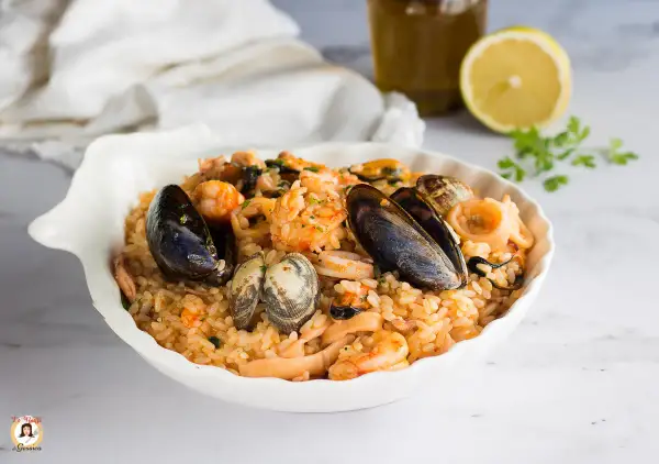 Un invitante risotto allo scoglio, ricco di cozze, vongole, gamberi e calamari, servito in una conchiglia bianca.