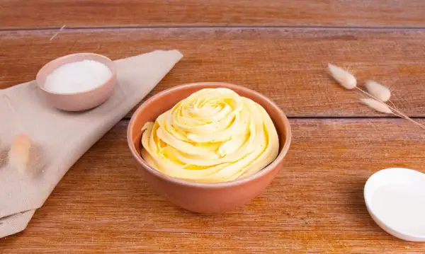Una ciotola di soffice crema al burro, pronta per decorare torte. Accanto, ciotoline con zucchero e decorazioni naturali.