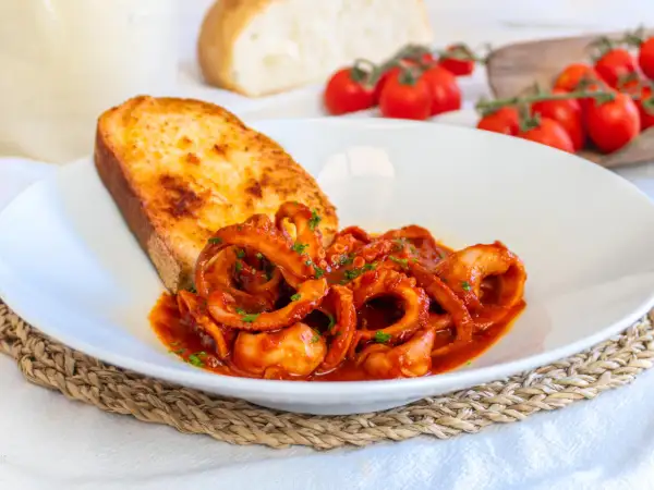 Un piatto di moscardini in umido, succulenti e profumati, accompagnati da una fetta di pane tostato e pomodorini freschi.