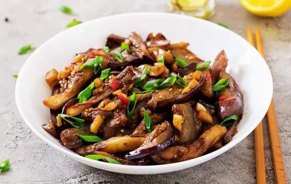 Melanzane in agrodolce, un piatto saporito con peperoncino, aglio e cipollotto, pronto per essere gustato con le bacchette.