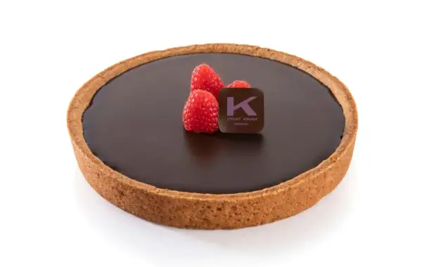 Una deliziosa crostata al cioccolato, con tre lamponi freschi e il logo di Ernst Knam.
