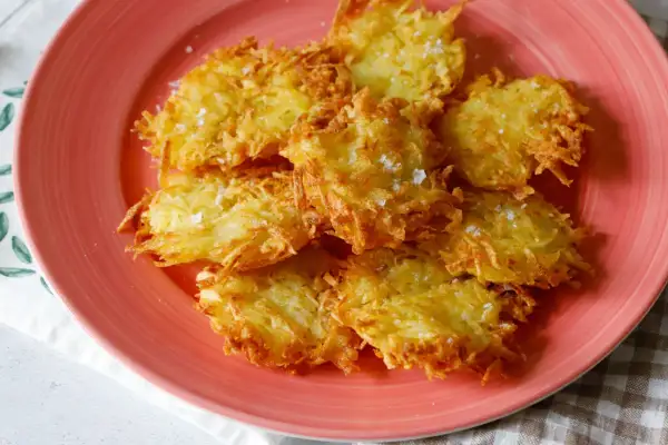 Tortel di patate dorati e croccanti, cosparsi di sale grosso, su un piatto rosa.