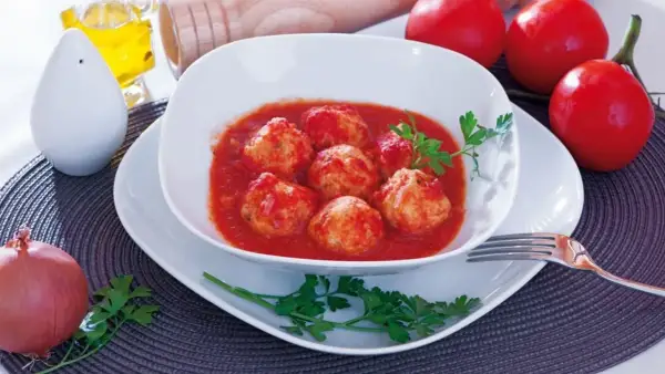 Polpette di merluzzo in salsa di pomodoro, guarnite con prezzemolo. Sullo sfondo, pomodori, cipolla e sale.