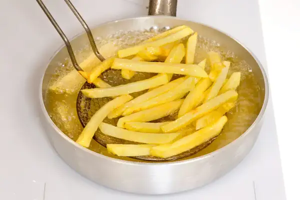 Patatine fritte dorate che sfrigolano nell'olio bollente, pronte per essere gustate.