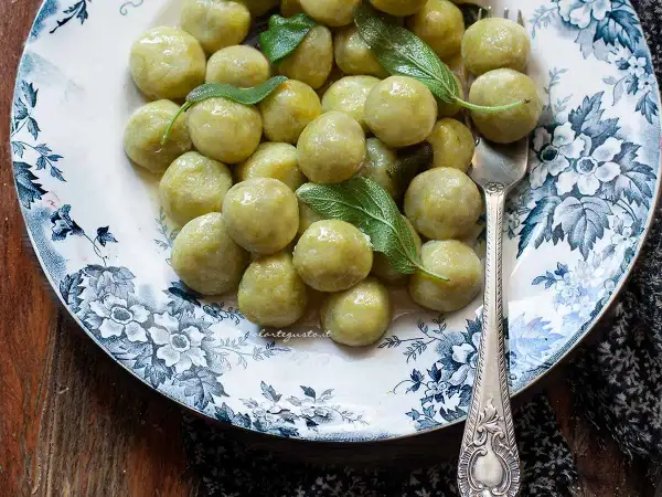 Un piatto di gnocchi di zucchine, conditi con burro e salvia, su un elegante piatto decorato.